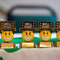 Eco-Schools celebration 5 Line of smiley face trophies which say "Well done!"