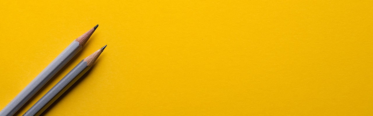 Two grey pencils on a bright yellow background