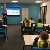 Picture 8 A classroom of primary school children watching a teacher present a powerpoint slide entitled common types of litter. Children on the right hand side of the classroom are wearing hi-vis jackets with the words Queensmead eco warriors.